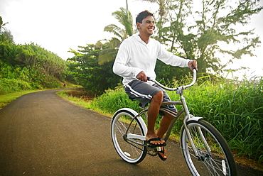 Hawaii, Kauai, Kealia Beach, Young man riding a bike on the bike path.