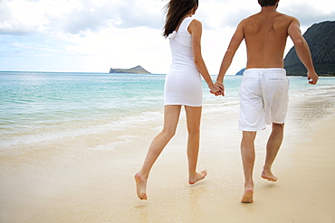 Hawaii, Oahu, Waimanalo, Young couple holding hands running together along the beach