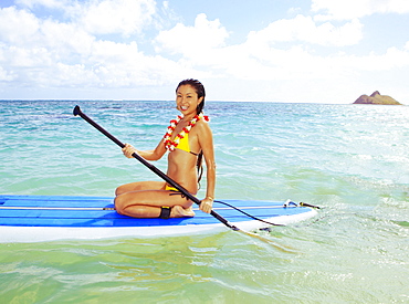 Hawaii, Oahu, Lanikai, Asian women paddle boarding off the beach near Mokulua Island.