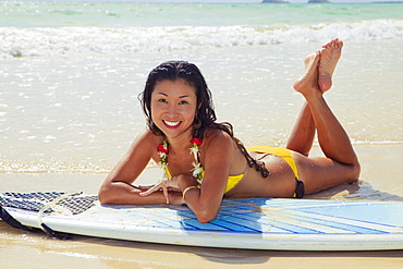 Hawaii, Oahu, Young woman poses with her surfboard on beach.