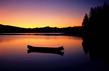 Alaska, Canoe floating on calm lake at sunset.