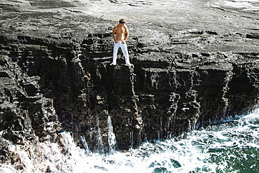 Hawaii, Oahu, Male wearing white pants on rocky cliff.