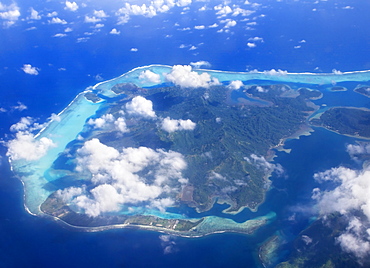 French Polynesia, aerial over atoll, view from above small white clouds outer barrier reef surrounds inner lagoon.