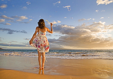 Hawaii, Maui, Woman standing on the shore of remote tropical location blowing bubbles.