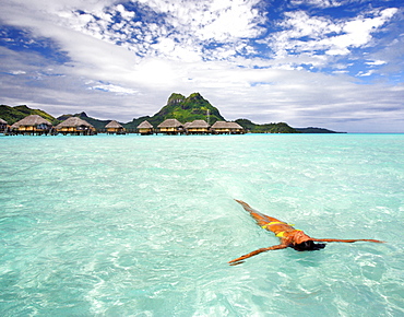 French Polynesia, Tahiti, Bora Bora, Woman floating in water near resort.