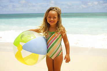 Hawaii, Oahu, little girl poses on beach with beach ball.