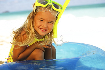 Hawaii, Oahu, little girl poses on beach with snorkel in blue tube.