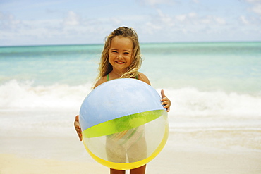 Hawaii, Oahu, little girl poses on beach with beach ball.