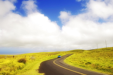 Hawaii, Big Island, South Kohala, Car driving down Saddle Road which curves through rolling grass hills near Waikii Ranch.