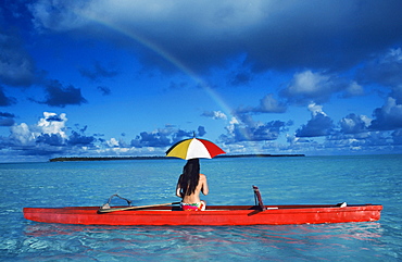 French Polynesia, Tetiaroa, Woman with umbrella in outrigger canoe floating on clear turquoise ocean, View from behind.