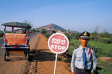 Cambodia, Lake Tonle Sap Village, Policeman standing beside road with stop sign.