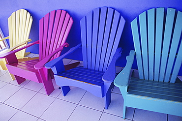 Cayman Islands, Grand Cayman, Colorful wooden chairs against purple wall of storefront.