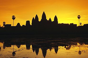 Cambodia, Siem Reap, Angkor Wat, silhouette of temple at sunrise, reflections on water surface, ornage sky