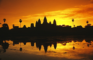 Cambodia, Siem Reap, Angkor Wat, silhouette of temple at sunrise, reflections on water surface, ornage sky