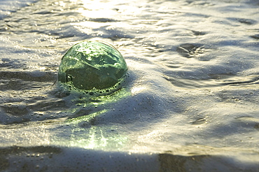 A glass fishing ball floats in shallow water, bright reflections