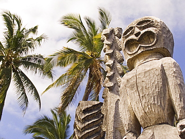 Hawaii, Big Island, Puuhonua O Honaunau, City of Refuge, Ki'i against blue sky and palm trees.