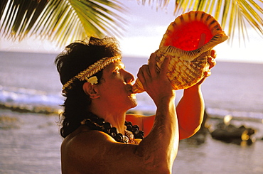 Hawaii, Native local Man at ocean blowing conch shell with shell haku