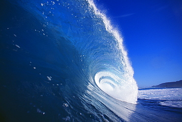 Blue wave curling, closeup side view with blue skies.