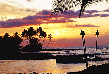 Hawaii, Big Island, Kohala, Waiulua Bay, Orange sunset with palm trees and tiki torches.