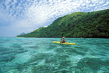 Fiji, Kadavu Islands, Woman kayaking in shallow water along coastline.