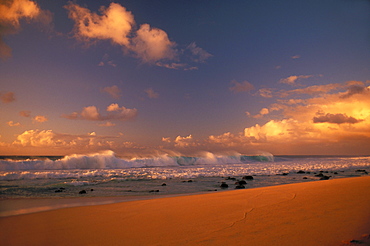 Hawaii, Oahu, Wave crashes on North Shore beach Sunset sky with fluffy warm clouds