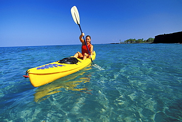 Female in red bathing suit paddling on kayak in crystal clear ocean