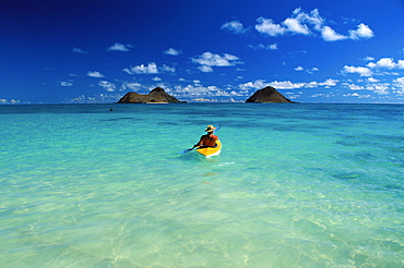 Hawaii, Oahu, Back view of man wearing hat on kayak heading to Mokulua Islands, blue skies