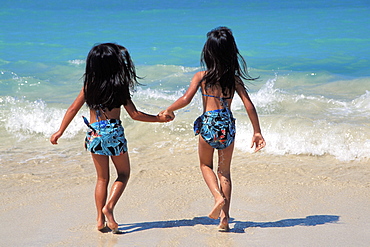 Hawaiian girls running into shoreline, view from behind, matching outfits