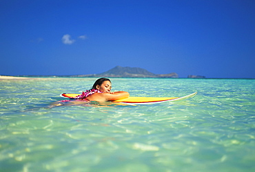 Hawaii, Oahu, Lanikai, Woman eyes closed resting head/arms on surfboard on clear water.