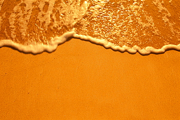 Shoreline water washes onto golden sand at sunset ,