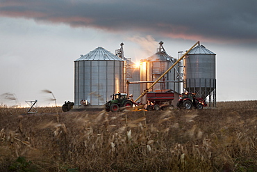 Grain silos and tractor under a dramatic sky at sunset, Quebec, Canada