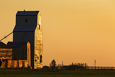 Wooden grain elevator refecting the orange glow of sunrise, Mossleigh, Alberta, Canada