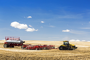 Tractor and air seeder in stubble field planting crop with blue sky and clouds, Alberta, Canada