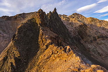 A shirtless hiker scrambles over a craggy ridge in the eastern Alaska Range near Whistler Creek in summer; Alaska, United States of America