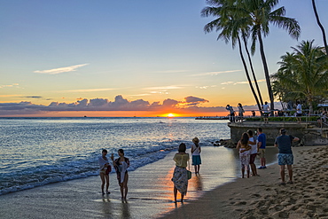 Tourists watch and photograph sunset on Waikiki Beach, Honolulu, Oahu, Hawaii, United States of America