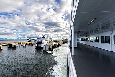 Looking over the railing of the passenger deck on BC ferries as the ship leaves the dock at Tsawwassen on a sunny day, another ship is currently in the dock, Vancouver, British Columbia, Canada