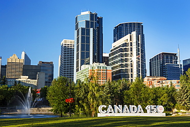 Canada 150 signage in city park with Calgary building towers in background with blue sky, Calgary, Alberta, Canada