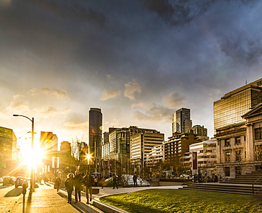 A street scene in Vancouver at sunset with pedestrians and buildings reflecting sunlight, Vancouver, British Columbia, Canada