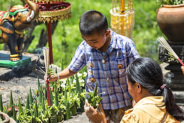 Boy with incense sticks by a Buddhist statue at the Vat Phou Temple Complex, Champasak, Laos