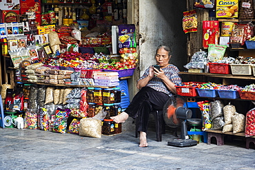 Female vendor sitting outside her shop with bare feet using her smart phone, Hanoi, Hanoi, Vietnam