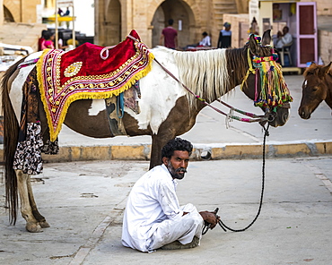 A man sits on the ground with his decorated horse standing beside him, Jaisalmer, Rajasthan, India