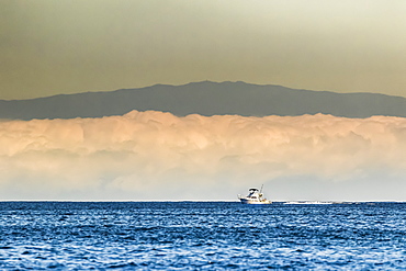 A sport fishing boat passes a morning fog bank off the Kona Coast, near Kailua on the Big Island, Hawaii during the summer, Island of Hawaii, Hawaii, United States of America