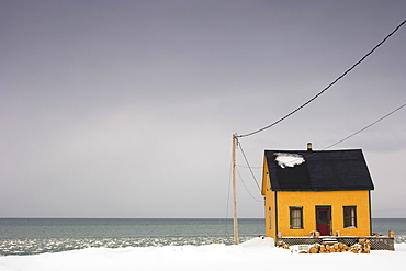 Small Yellow House On The Water's Edge In Winter, Quebec, Canada