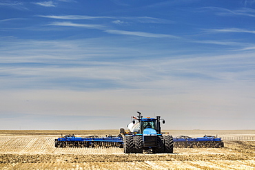 Tractor with air seeder, seeding a stubble field with blue sky and hazy clouds, near Beiseker, Alberta, Canada