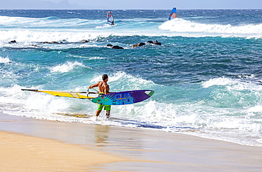 Three windsurfers, one standing on the beach at the water's edge looking out, Kihei, Maui, Hawaii, United States of America