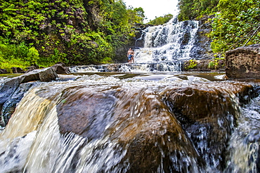 A young couple standing in front of a waterfall on private land on the island of Kauai, Kauai, Hawaii, United States of America