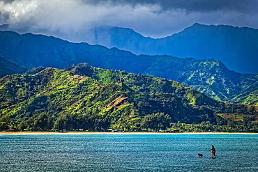 A man and his dog on a stand up paddle board in Hanalei Bay with mountains in background, Hanalei, Kauai, Hawaii, United States of America