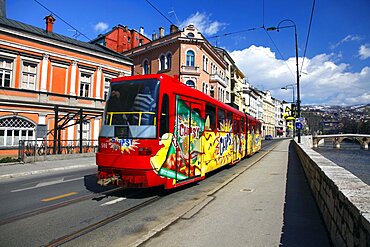 Red and yellow tram on bank of Miljacka River and Latin Bridge, Sarajevo, Bosnia and Herzegovina, Europe