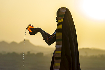 Ahir Woman in traditional colorful cloth pouring water at sunset, Great Rann of Kutch Desert, Gujarat, India, Asia