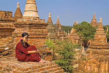 Young Burmese woman in a red dress sitting on the roof of a temple, Bagan (Pagan), Myanmar (Burma), Asia 